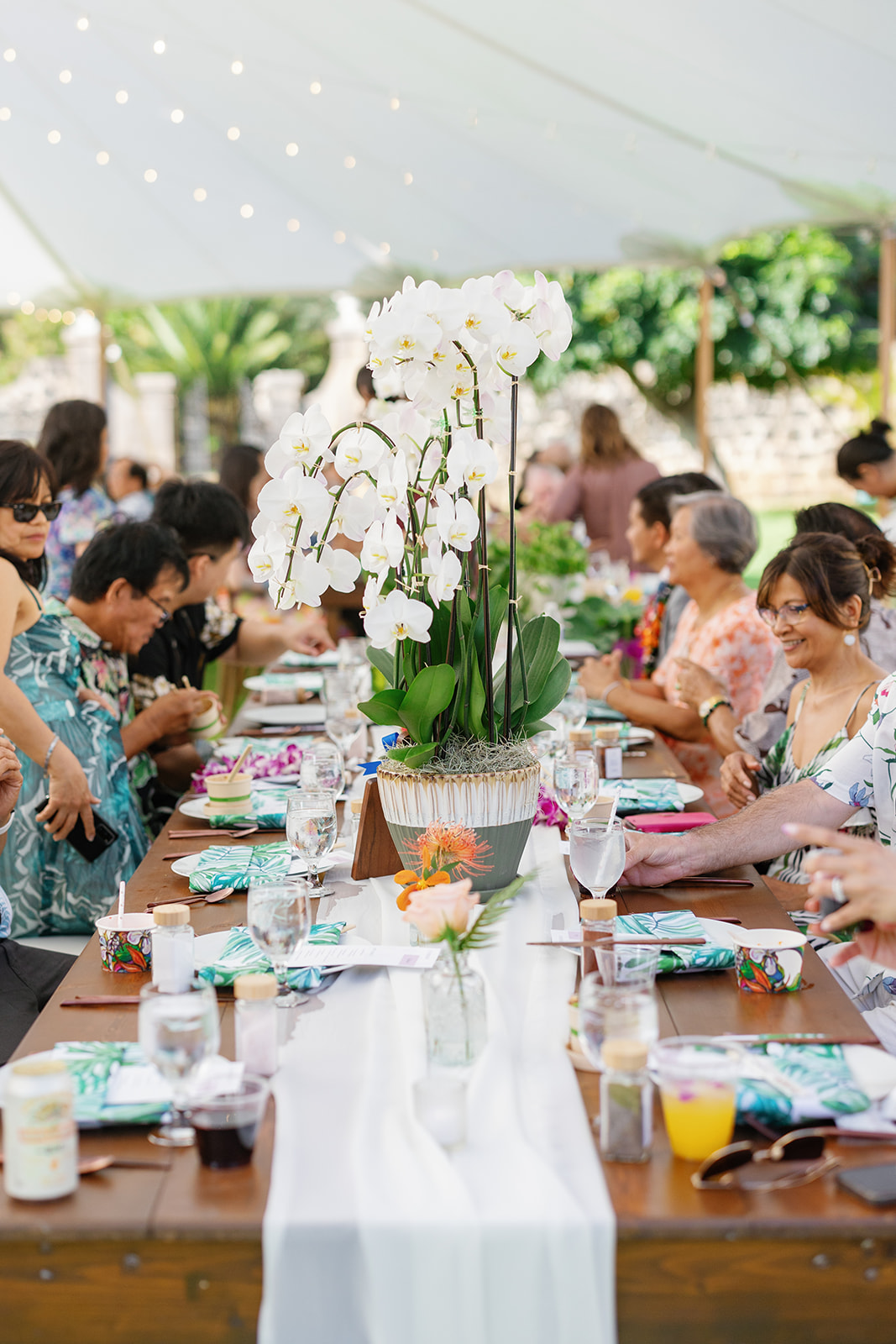 a long wooden table decorated for a wedding reception underneath a white tent 