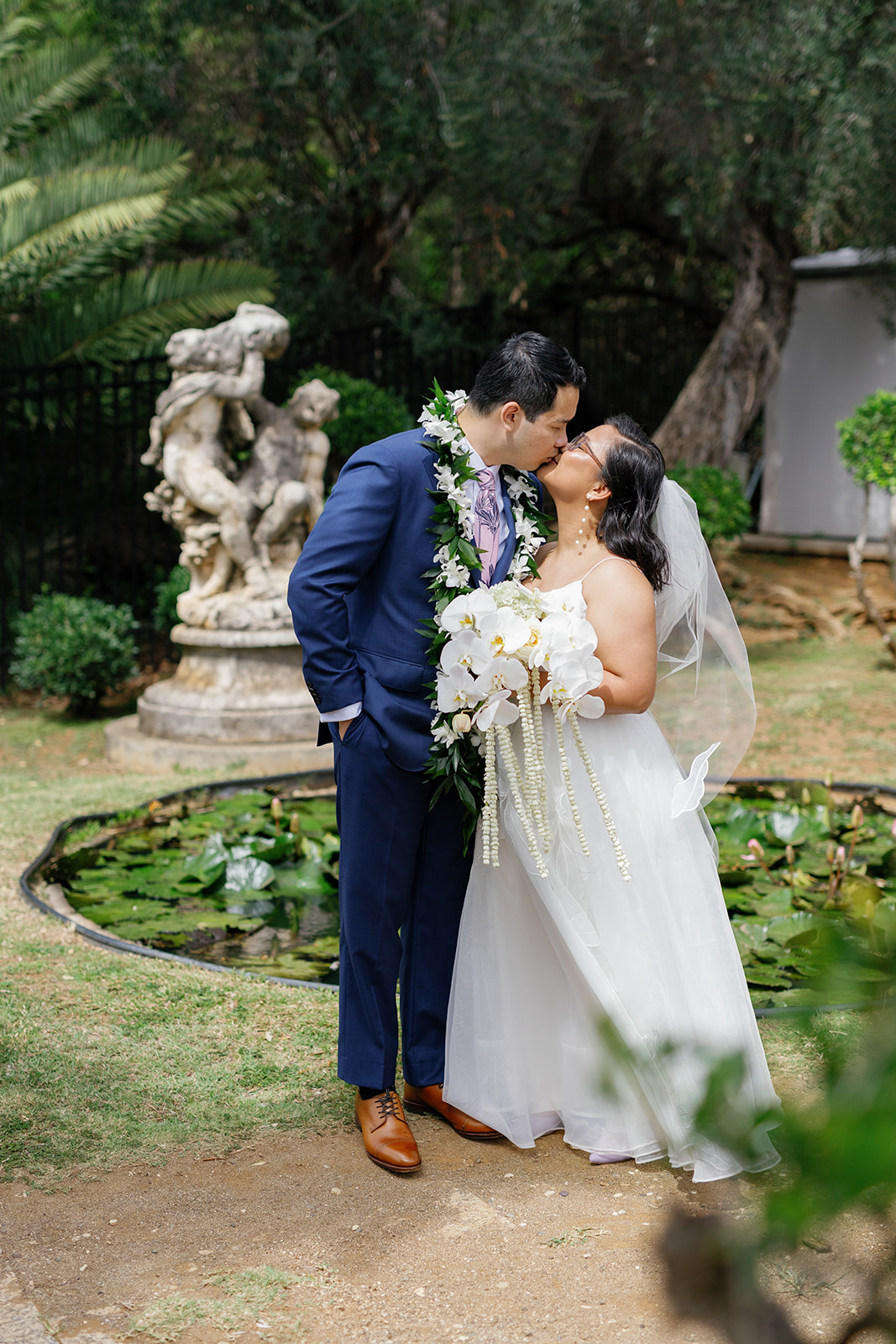 a couple kissing next to a pond and statues on the day of their wedding 