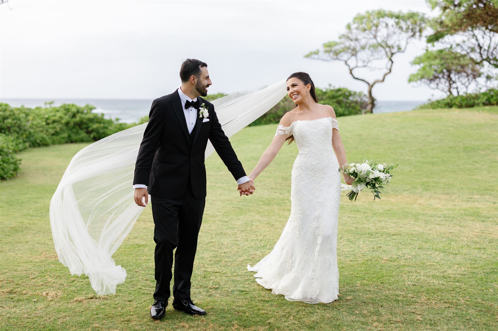 a couple on the day of their wedding walking hand in hand on a lawn at Ritz-Carlton O'ahu, Turtle Bay