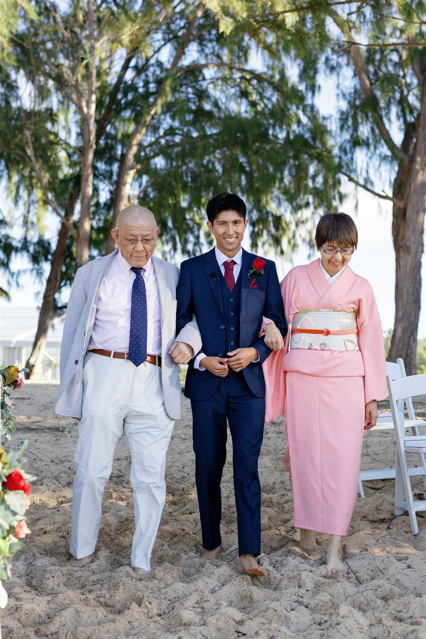 a man walking in the sand with is parents for his wedding ceremony
