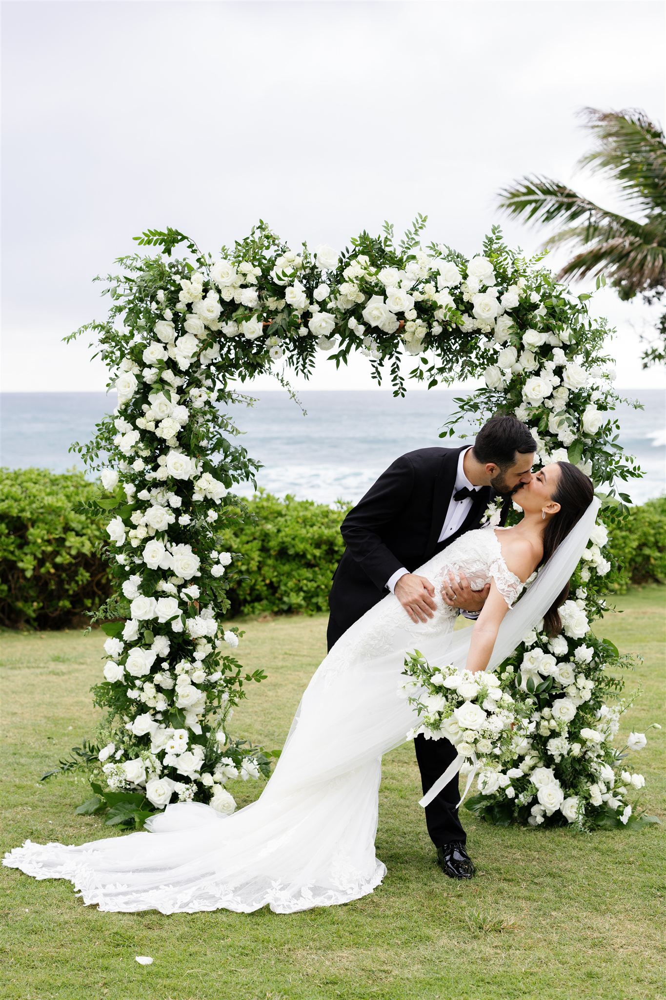 a groom dipping his bride in front of a floral arch next to the ocean at their wedding ceremony at Ritz-Carlton O'ahu, Turtle Bay