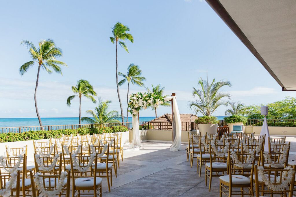 A wedding ceremony on a terrace with a white floral arrangement on a wooden arch at the end of the aisle 