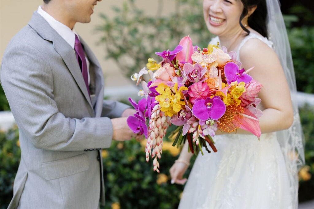 A close up of a newlywed holding a colorful bouquet of flowers with their partner standing next to them 