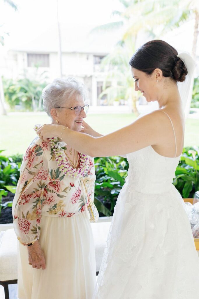 a person in a wedding dress placing a lei over an elderly family member 