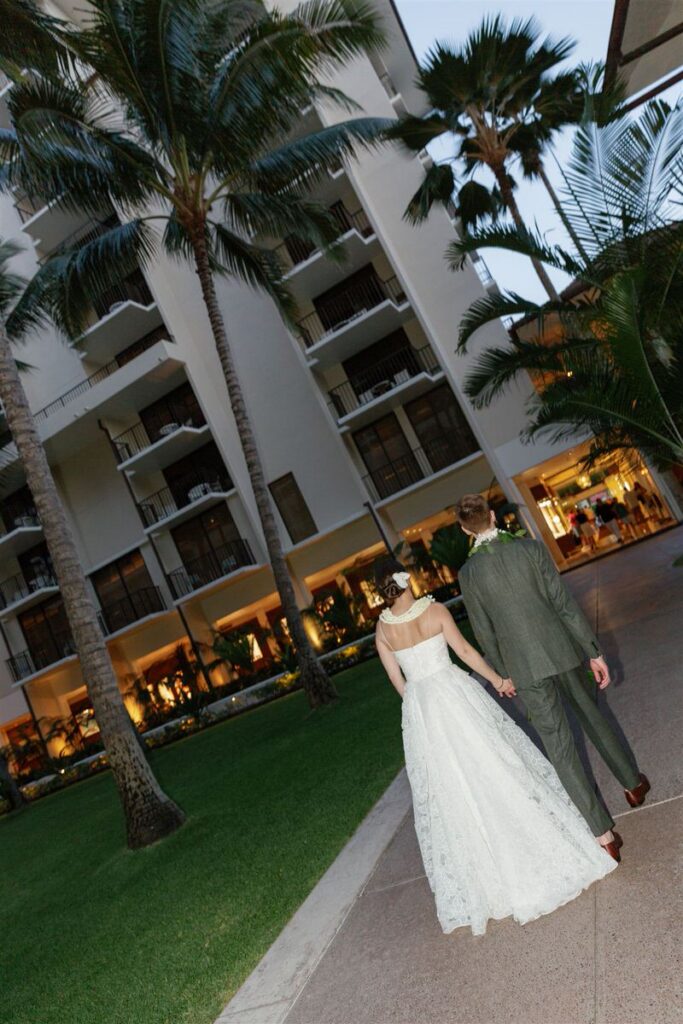 A newlywed couple holding hands and walking towards a hotel 