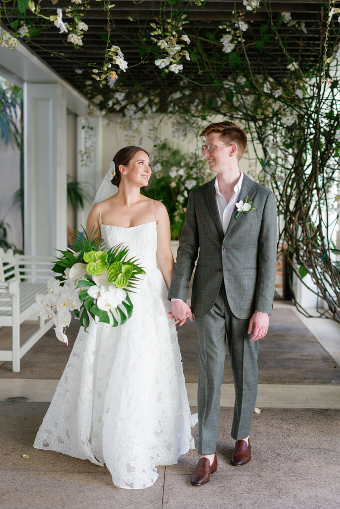Newlyweds holding hands and smiling at each other as they walk together 