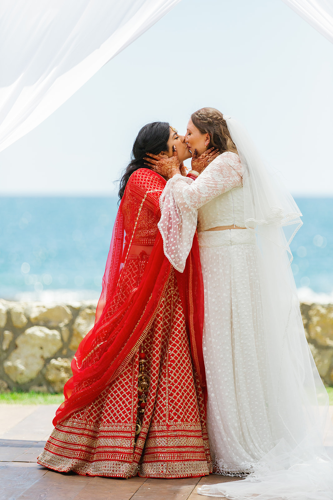 two women kissing during their wedding cermeony at  the Four Seasons Resort on Oahu next to the ocean 