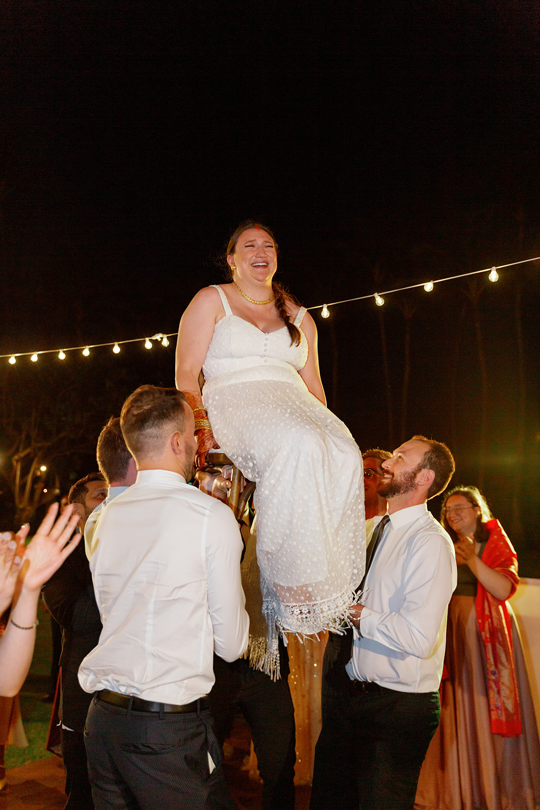 a group of men lifting a woman into the air on a chair during her wedding reception 