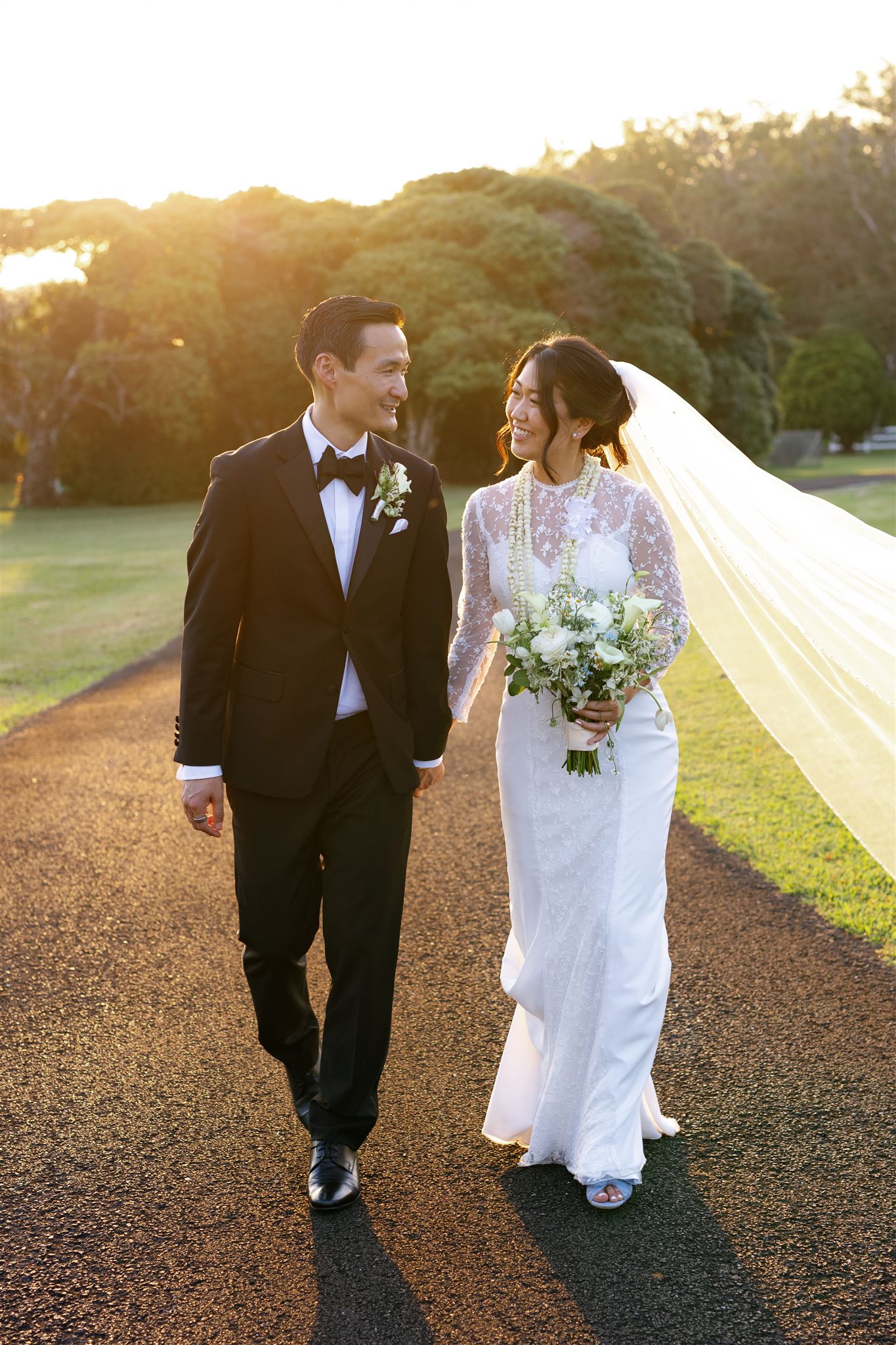 a bride and groom holding hands and smiling at each other taking golden hour portraits 