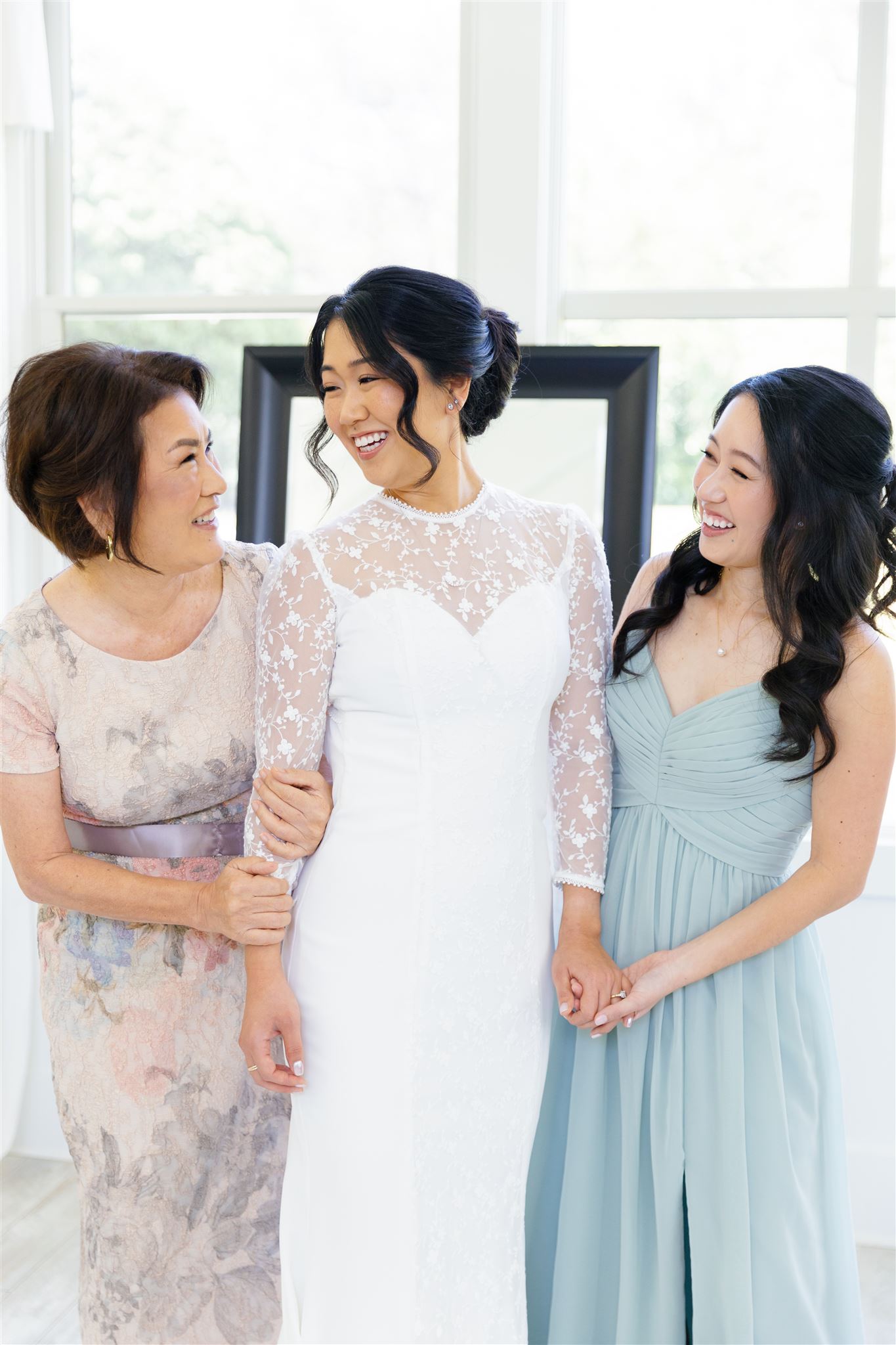 a bride smiling at her mother and her sister is next to her holding her hand 