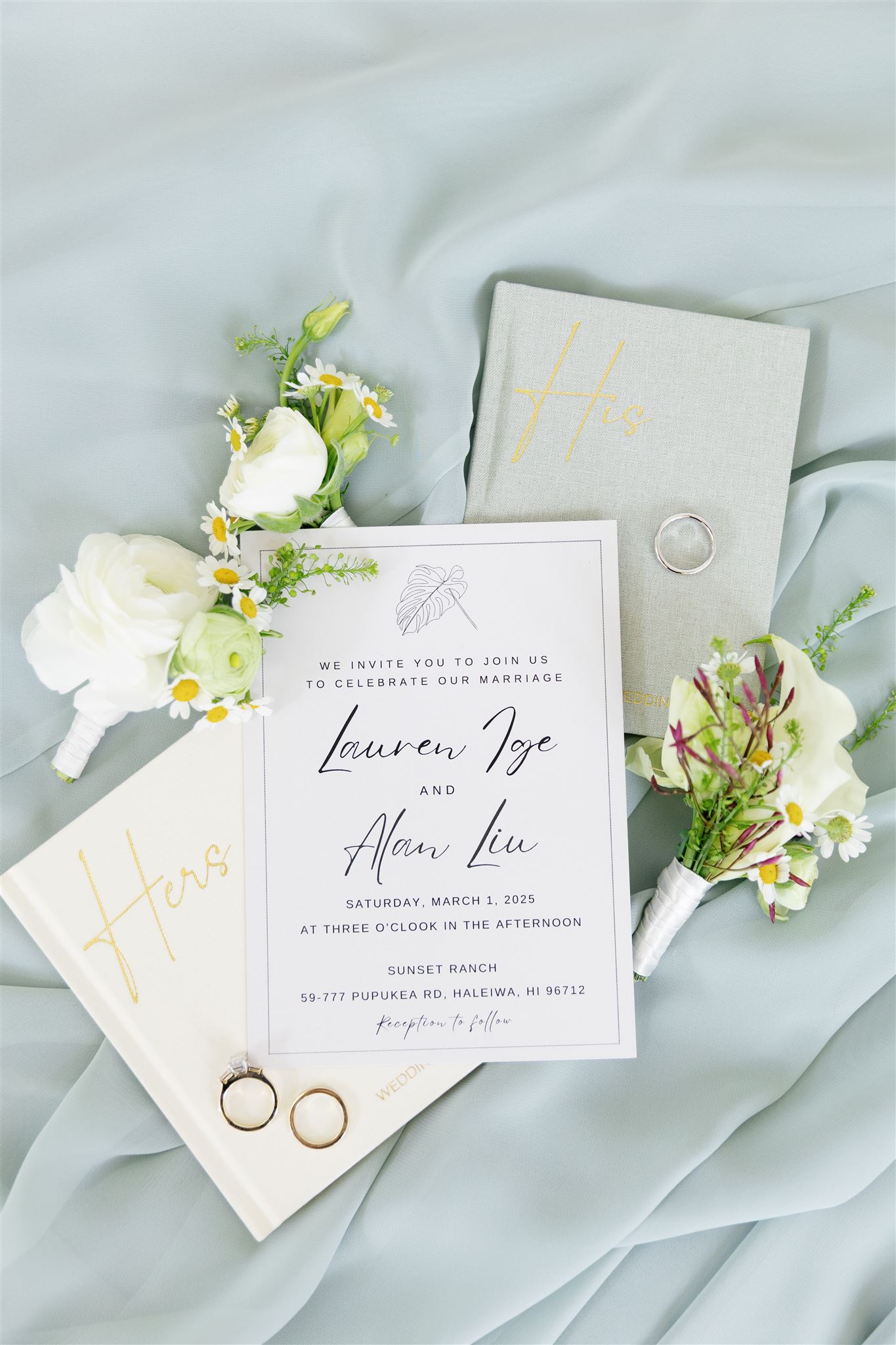 a wedding detail flatlay with wedding invitations, his and her vow books, rings, and flowers 