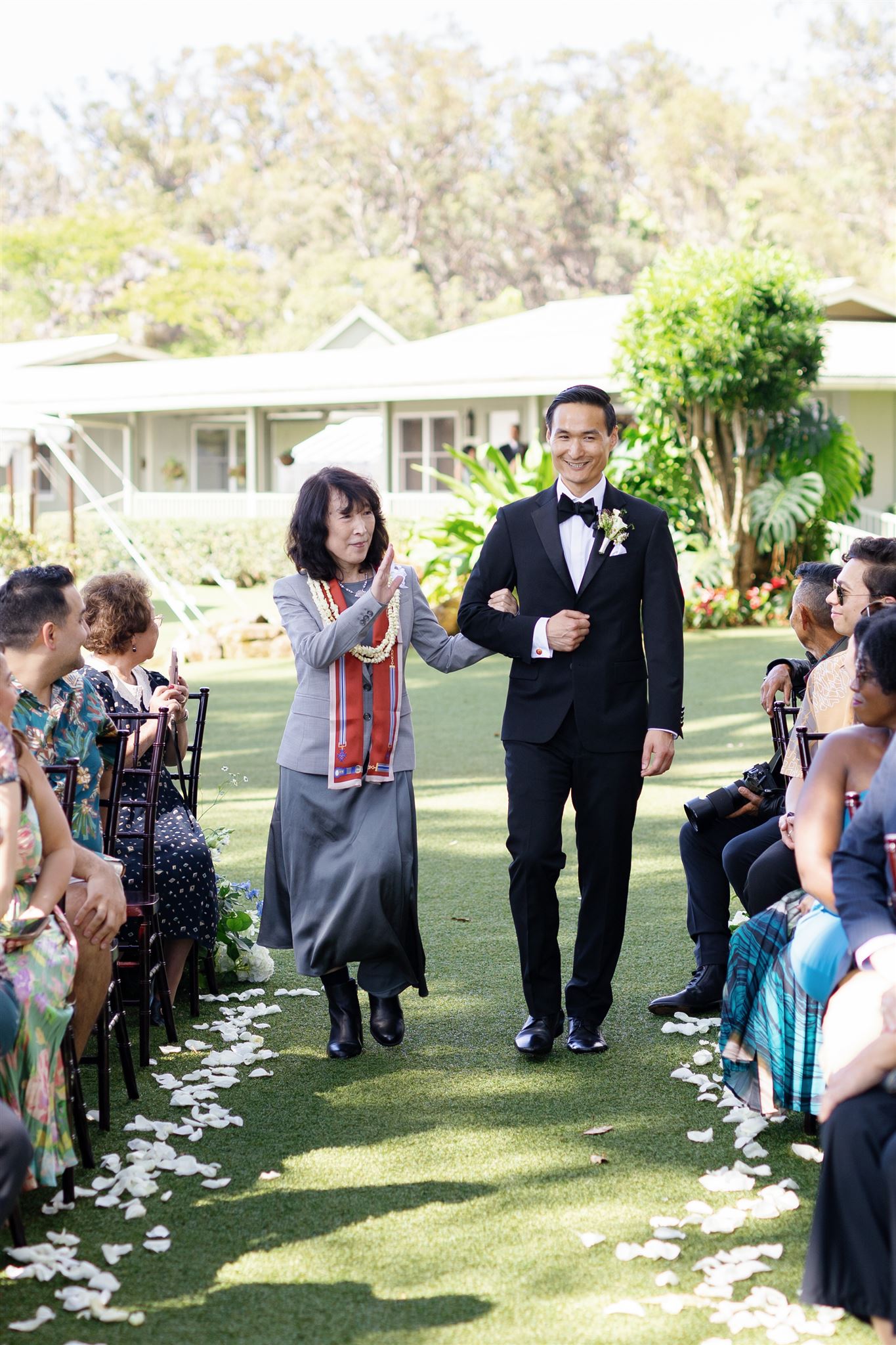 a groom walking arm in arm with his mother down the aisle 