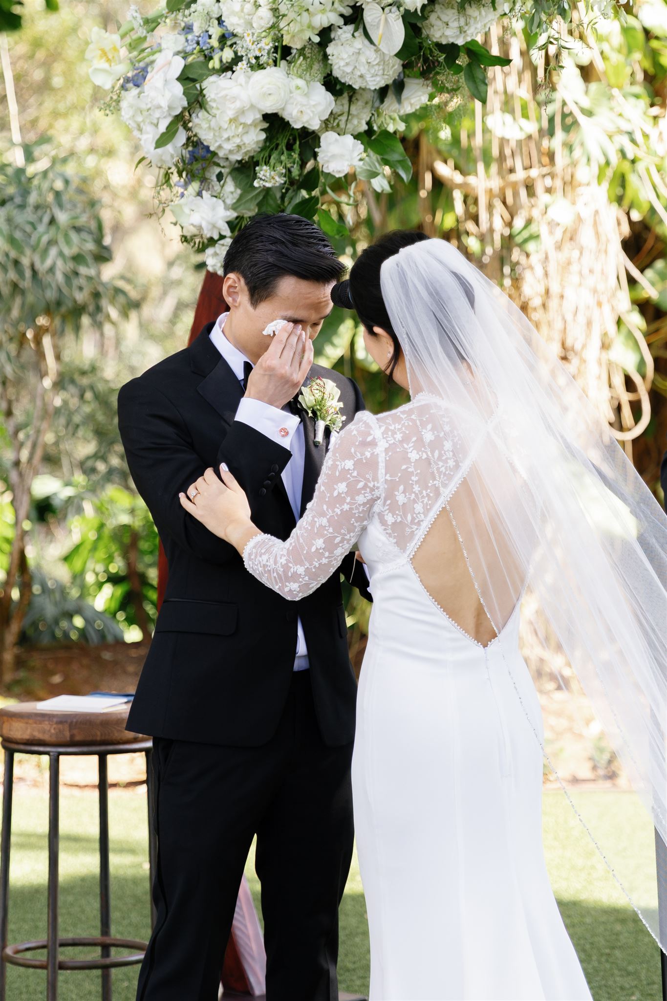 a groom getting emotional during his wedding ceremony at sunset ranch in hawaii as his bride comforts him 