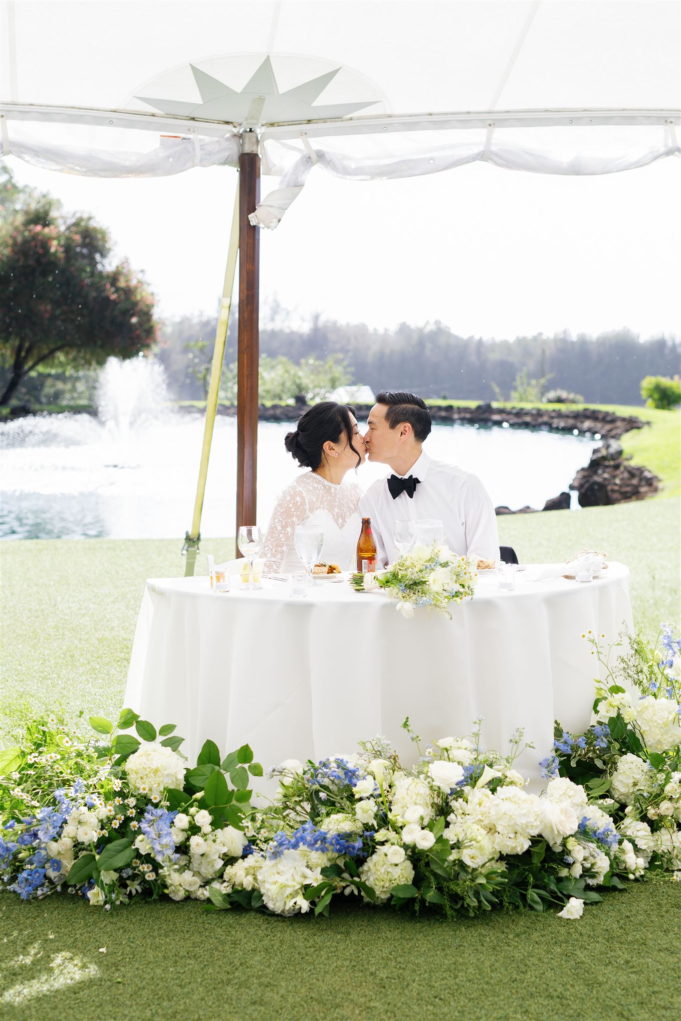 a bride and groom kissing at their reception underneath of a white tent next to a pond 