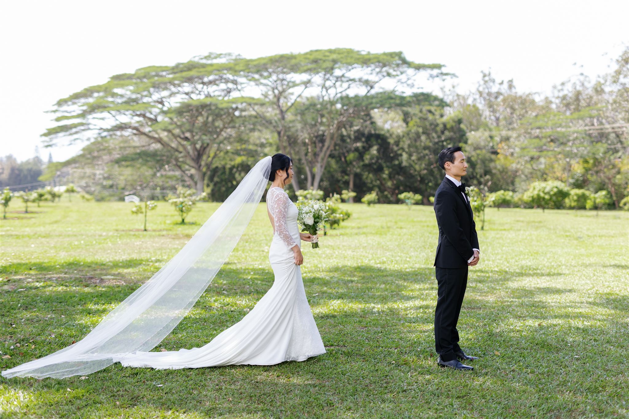 a bride walking towards her partner on the lawn of sunset ranch in hawaii who is about to share a first look with him