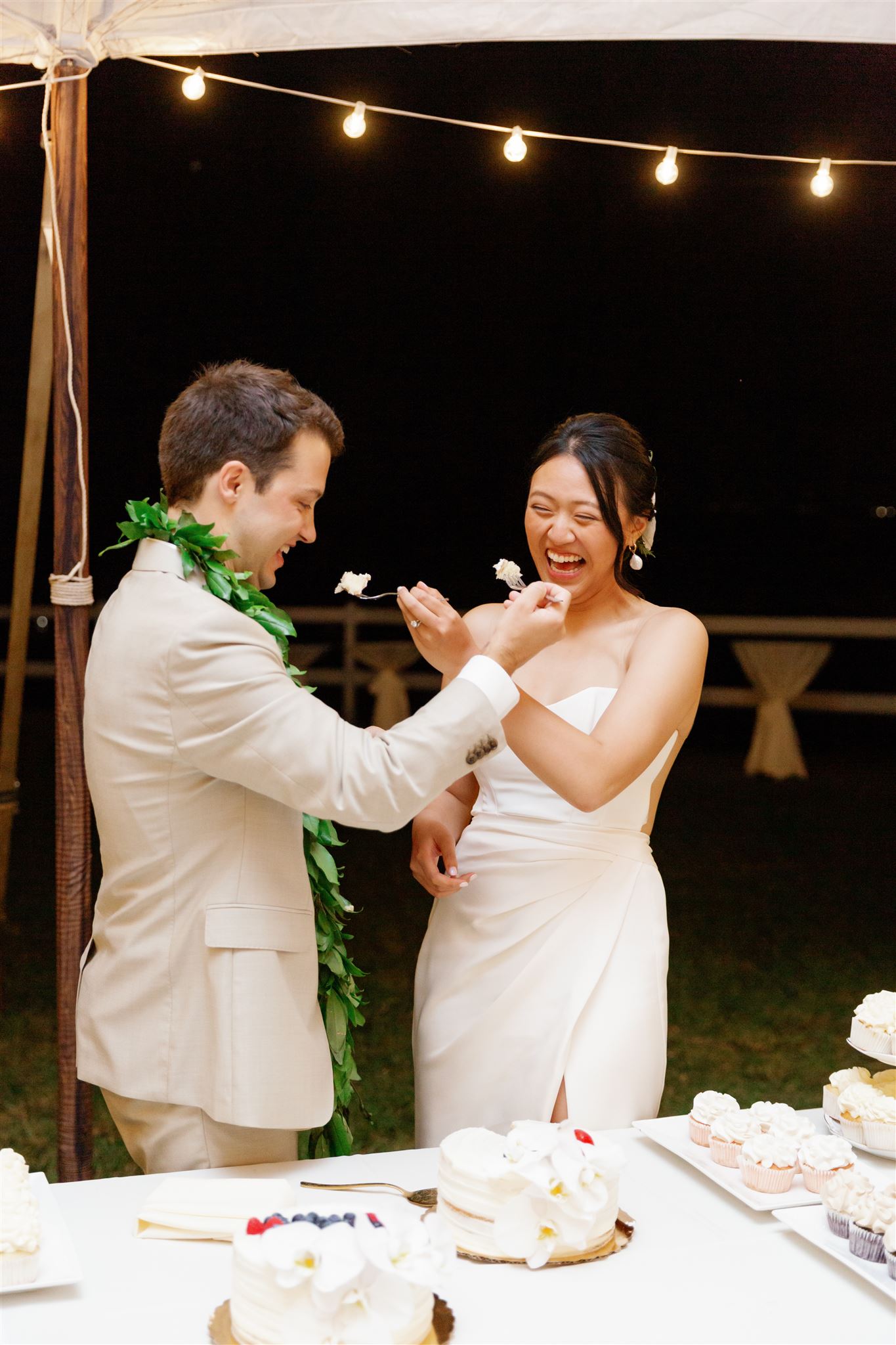 a bride and groom feeding each other cake at their wedding reception at Paliku Gardens at Kualoa Ranch