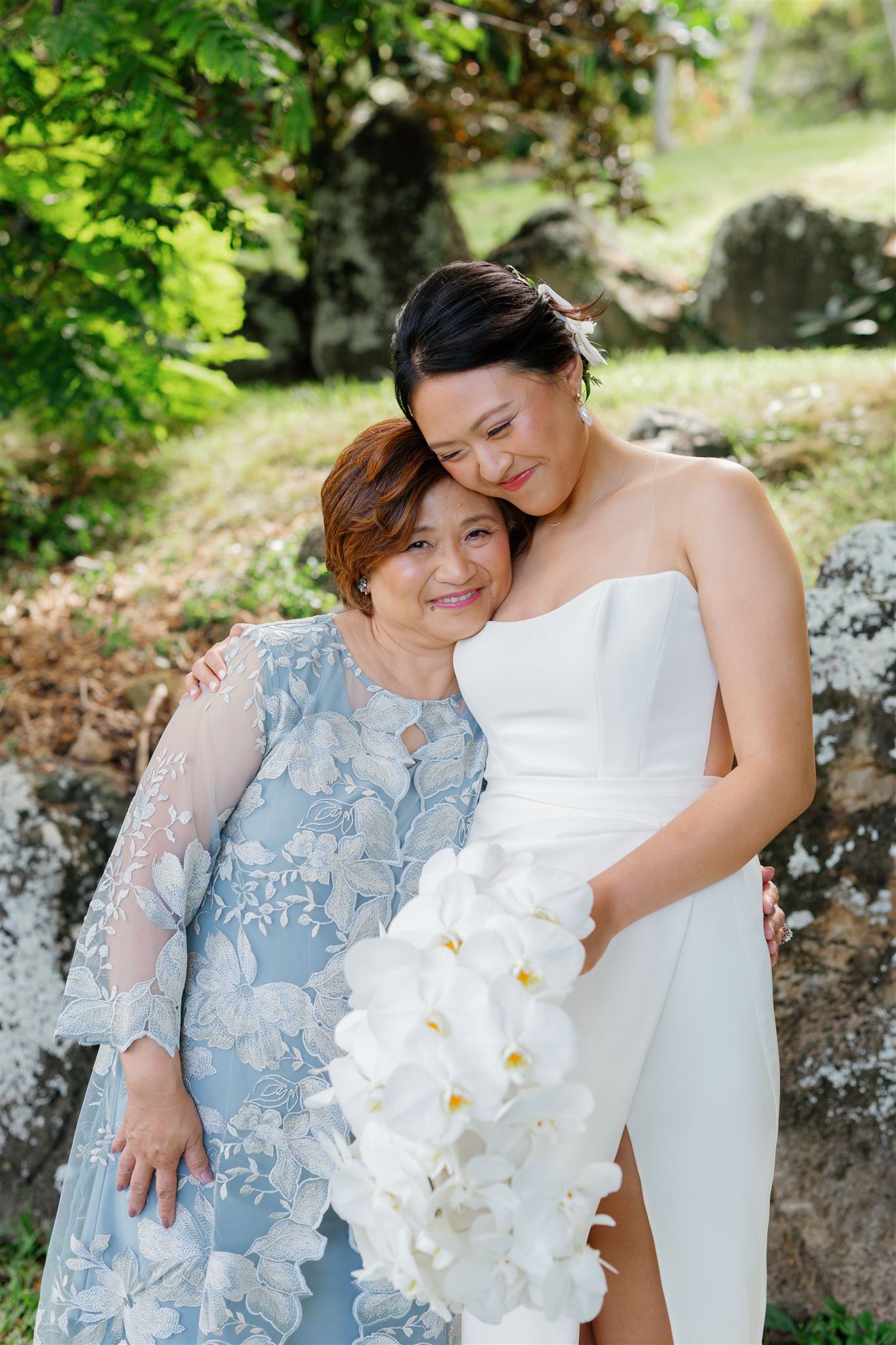 a bride holding a bouquet of white orchids hugging her mother 
