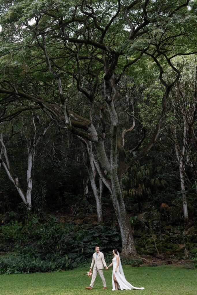 a bride and groom walking and holding hands in waimea valley
