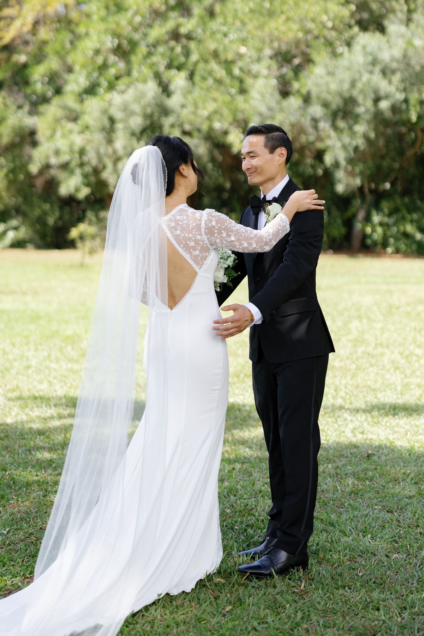 a bride and groom sharing a first look in a field surrounded by trees