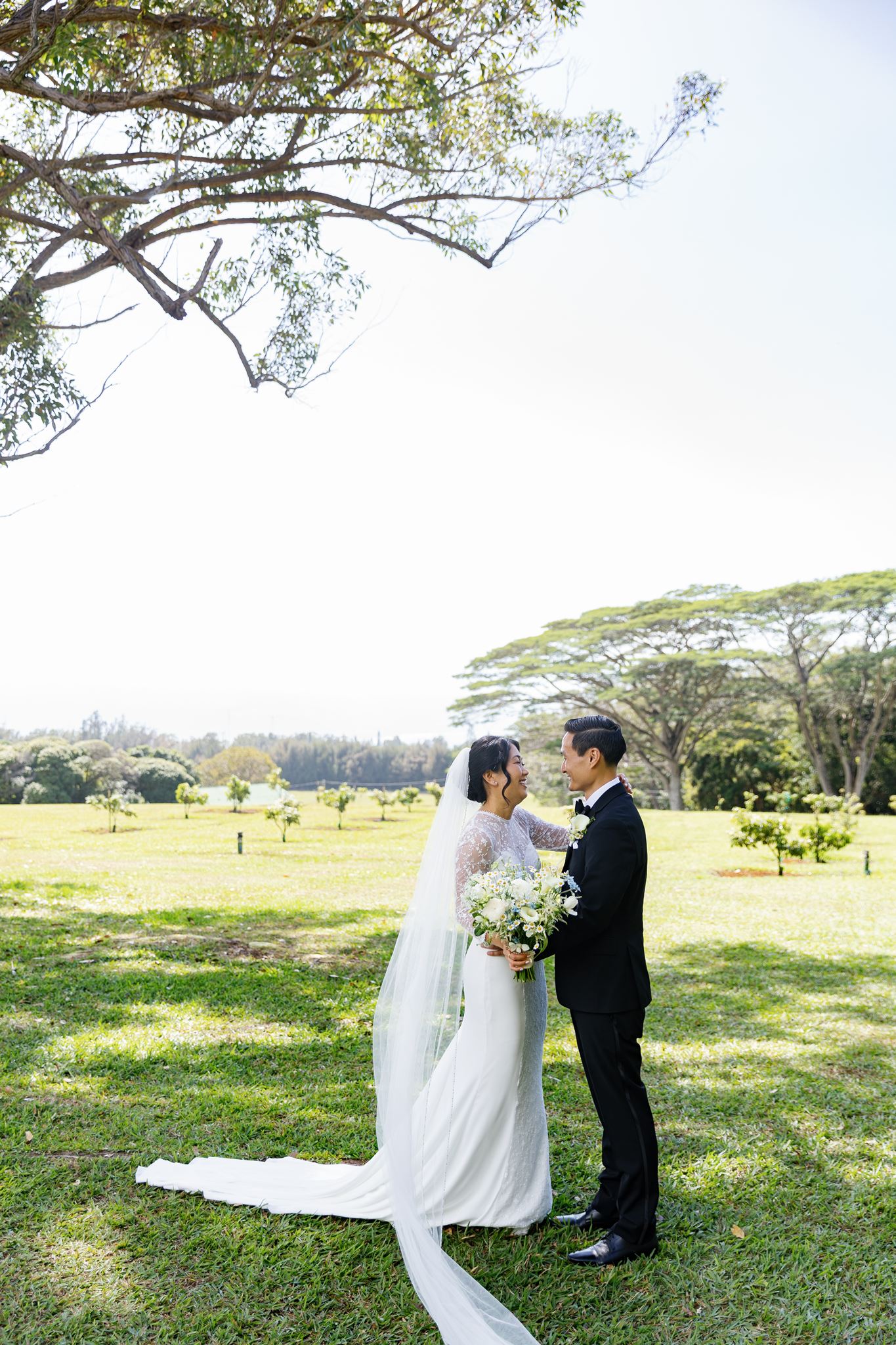 a bride and groom taking wedding portraits in a field the bride is touching the groom's shoulder and they are both laughing