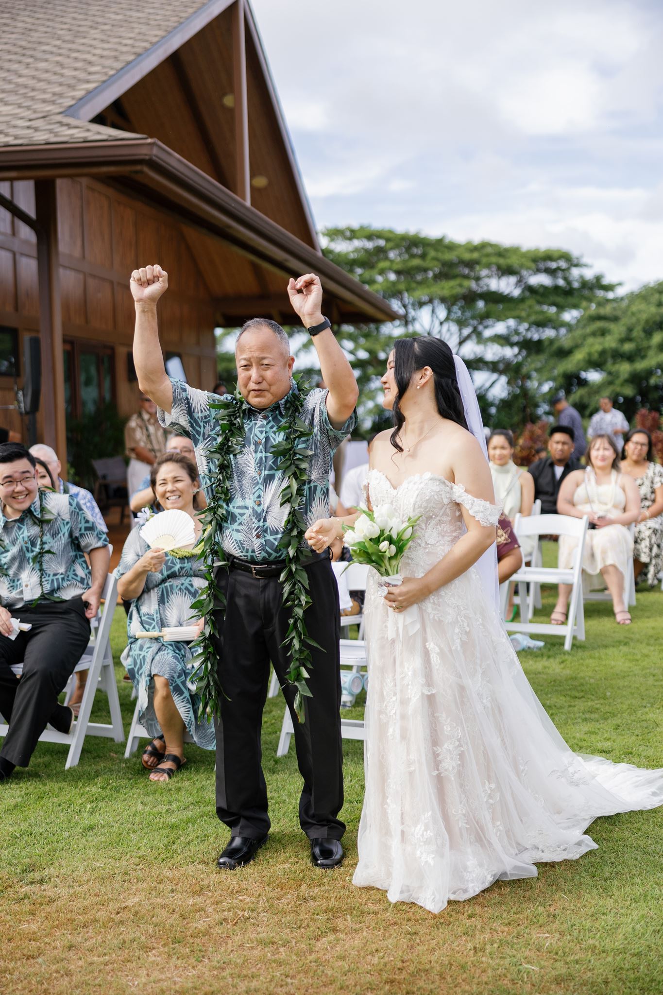 a bride walking down the aisle with her dad who is lifting his arms up in the air in excitement as their wedding guests watch them