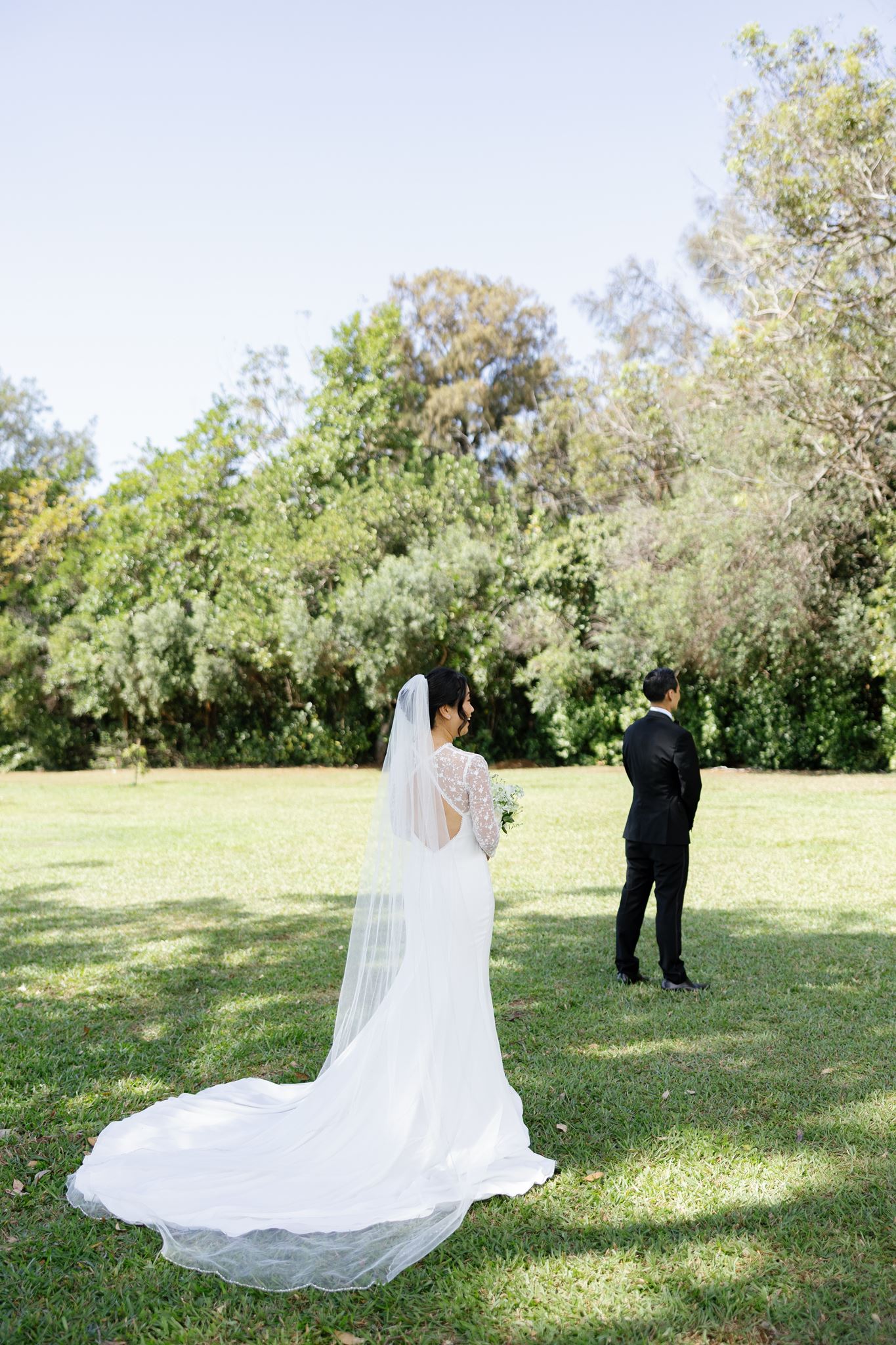 a bride standing in a field behind her fiance about to share a first look with him on their wedding day