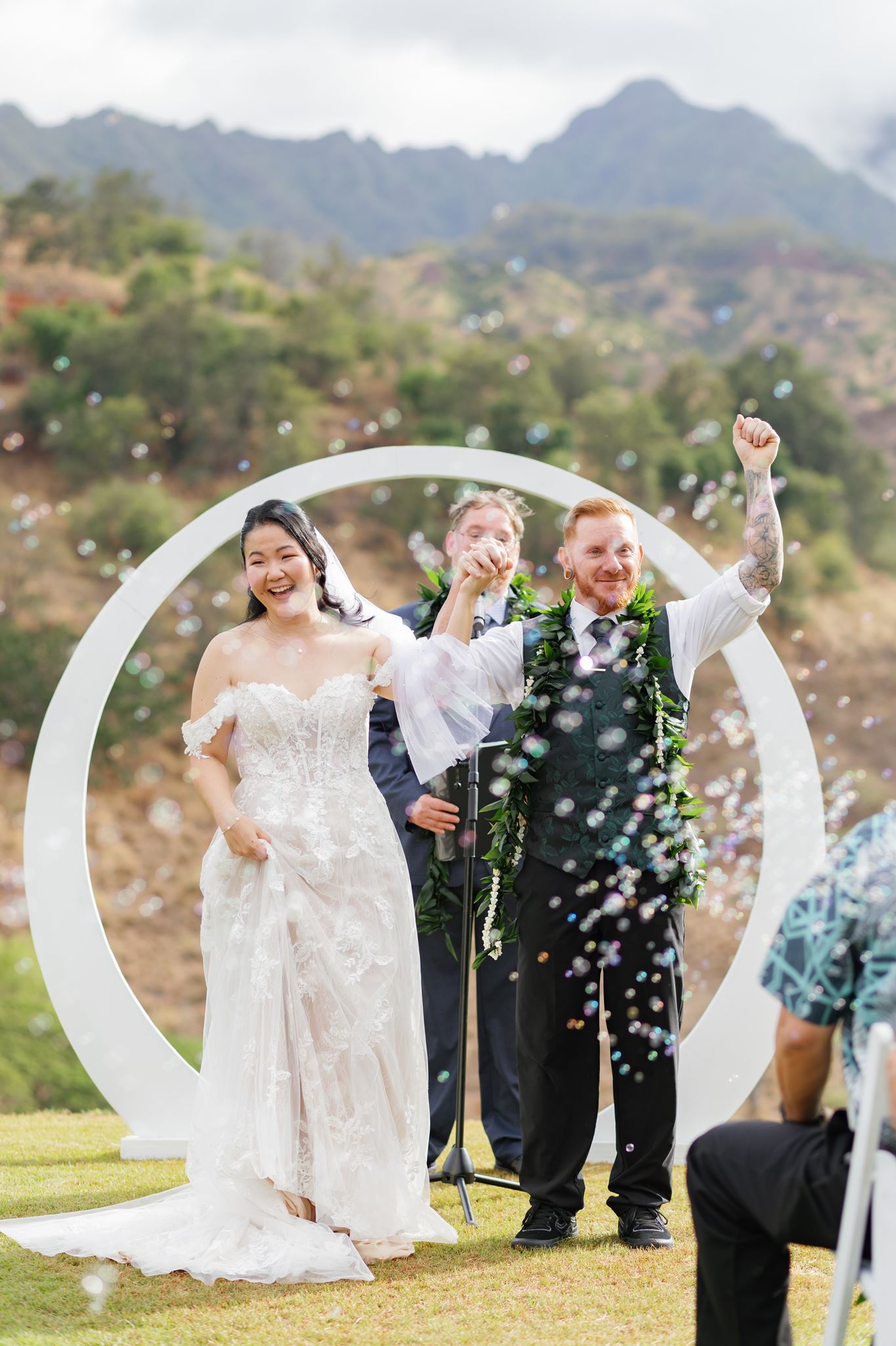 a husband and wife cheering after they finish their wedding ceremony as their guests blow bubbles