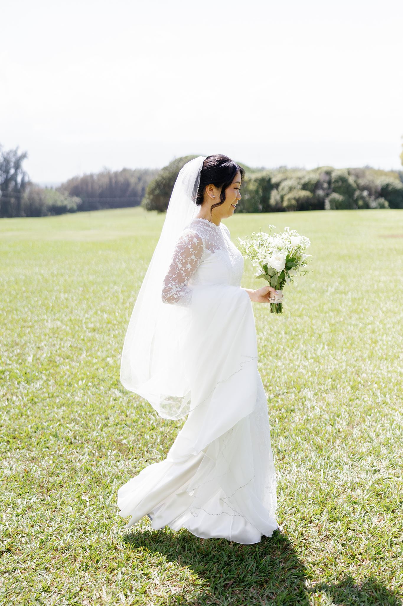 a bride walking through a field holding a bouquet of white flowers
