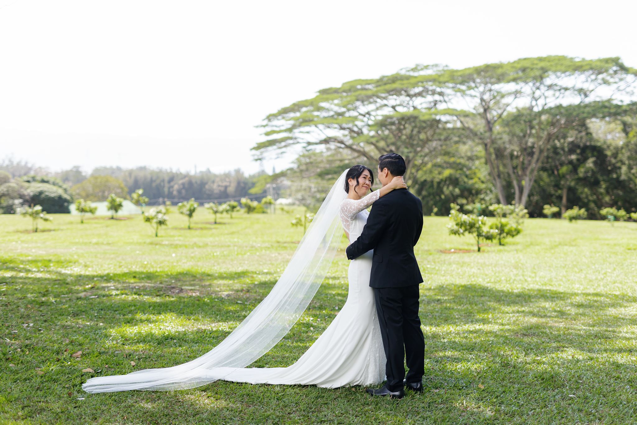 a bride and groom embracing in a field after sharing a first look together the bride has her hands around the groom's neck and is softly smiling at him