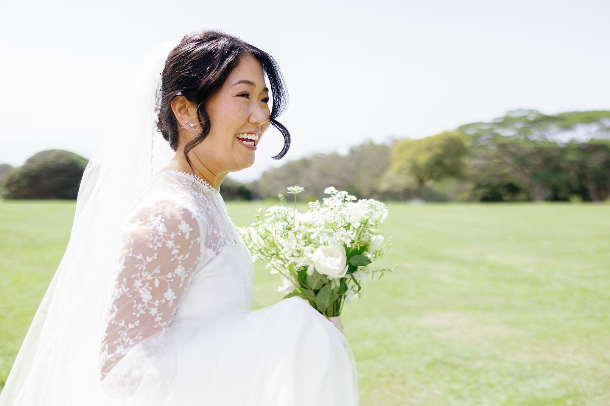 a bride laughing as she walks through a field holding a bouquet of white flowers