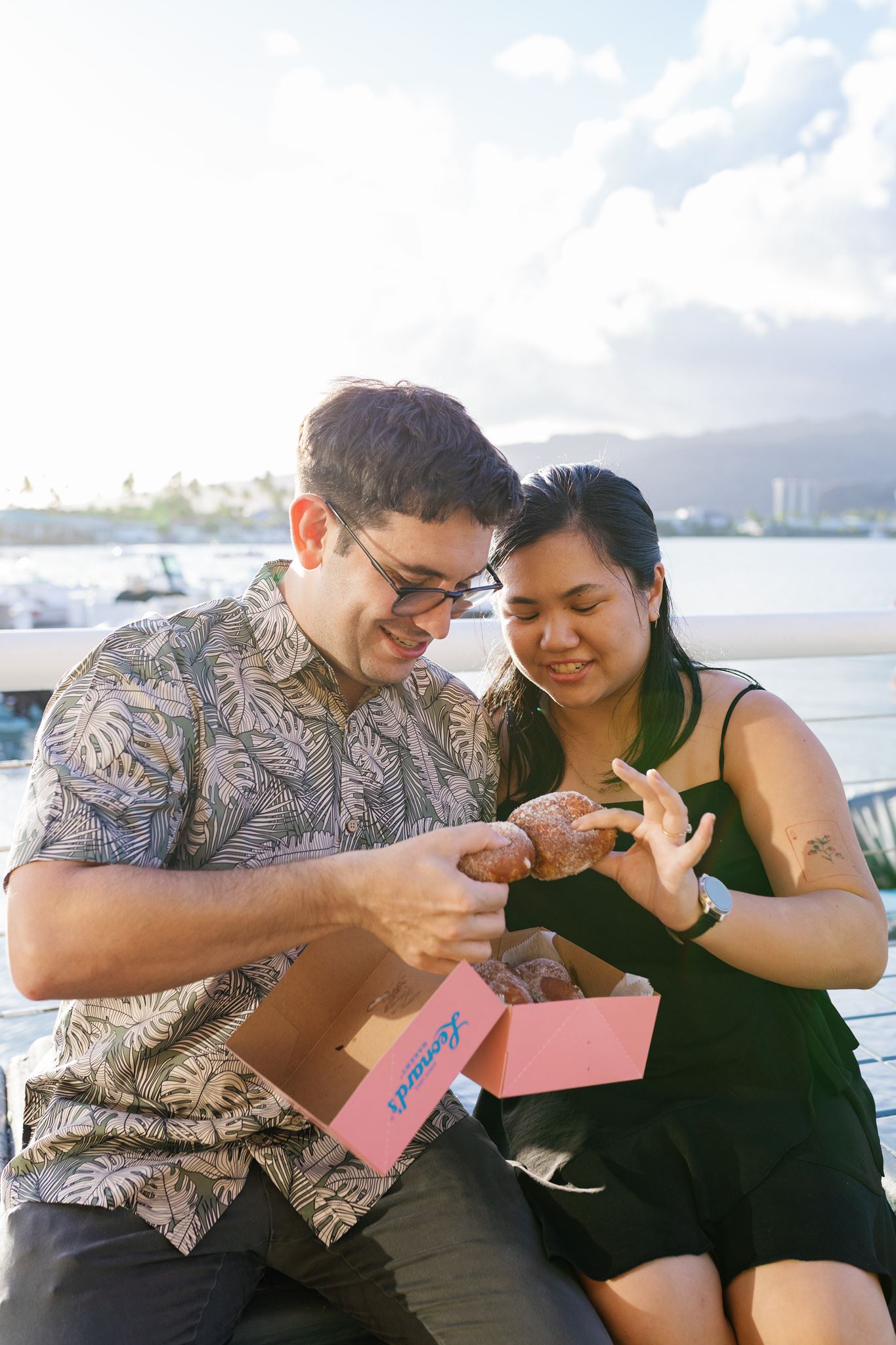 a man and woman eating donuts from leonards during their hawaii engagement session