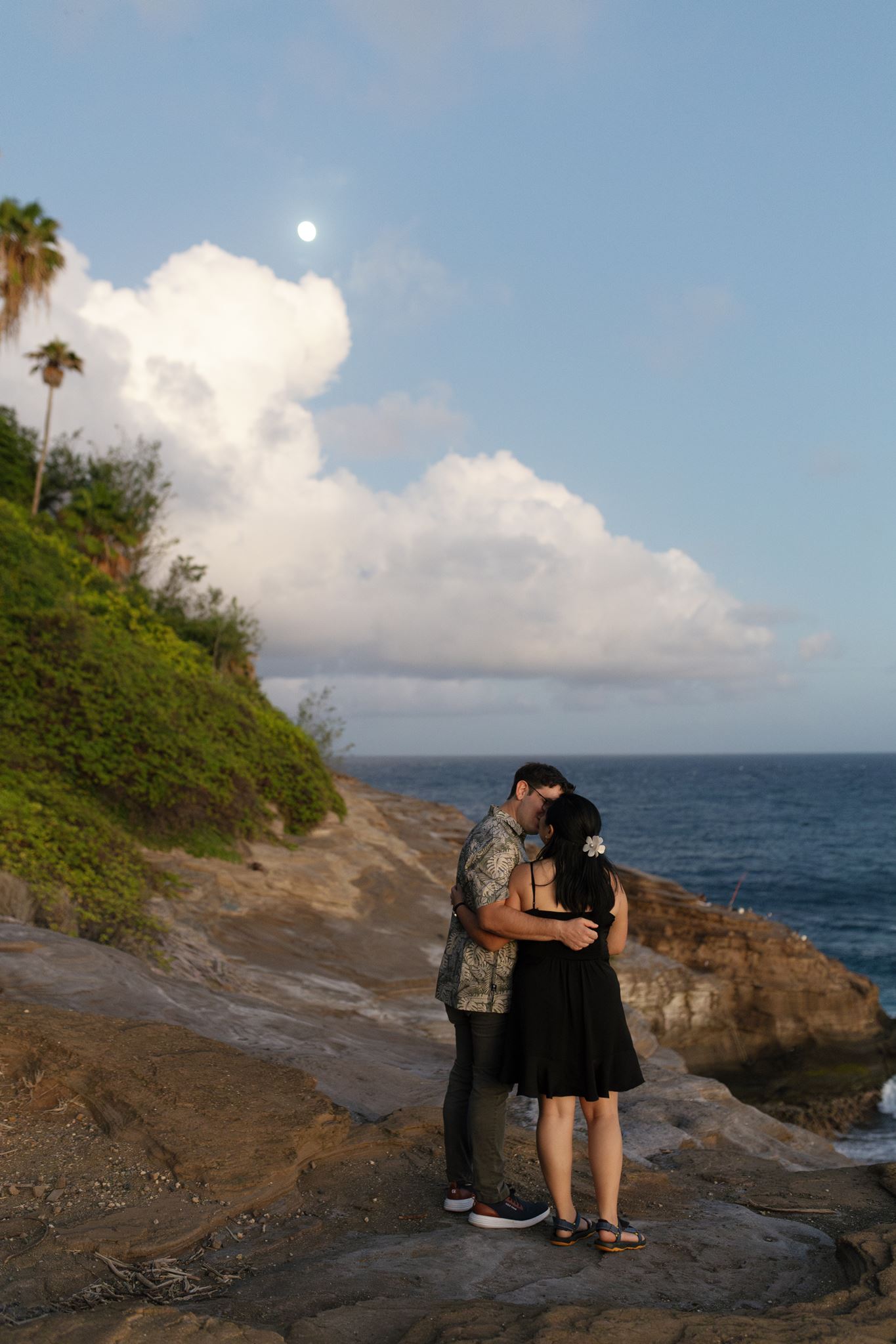 a man and woman kissing next to the ocean during their engagement session at sunset.