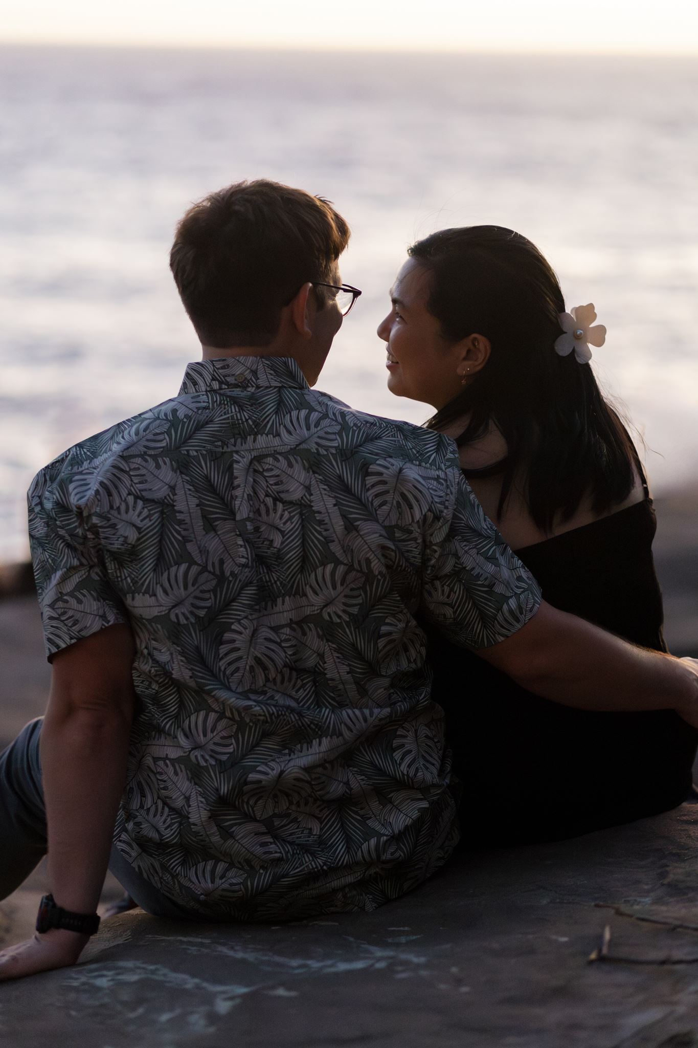 a man and woman sitting next to each other looking out at the ocean at sunset