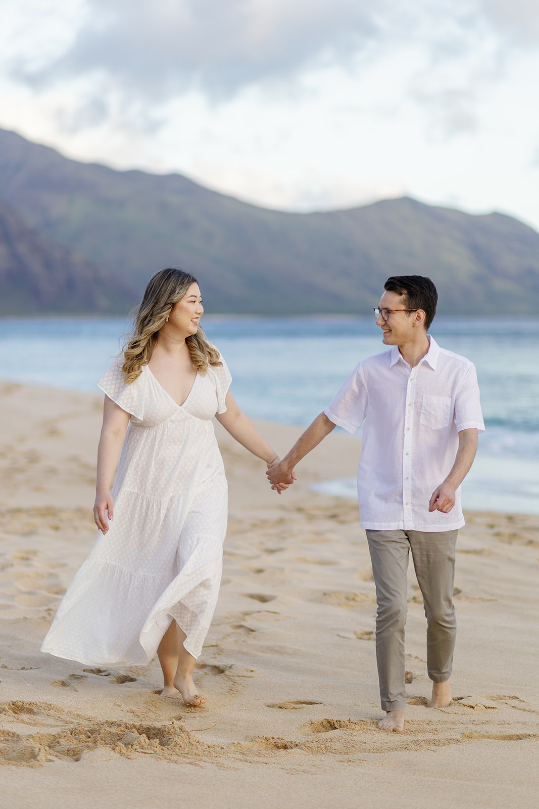 a couple having an engagement session on the beach in hawaii at sunset they are holding hands and walking together in the sand