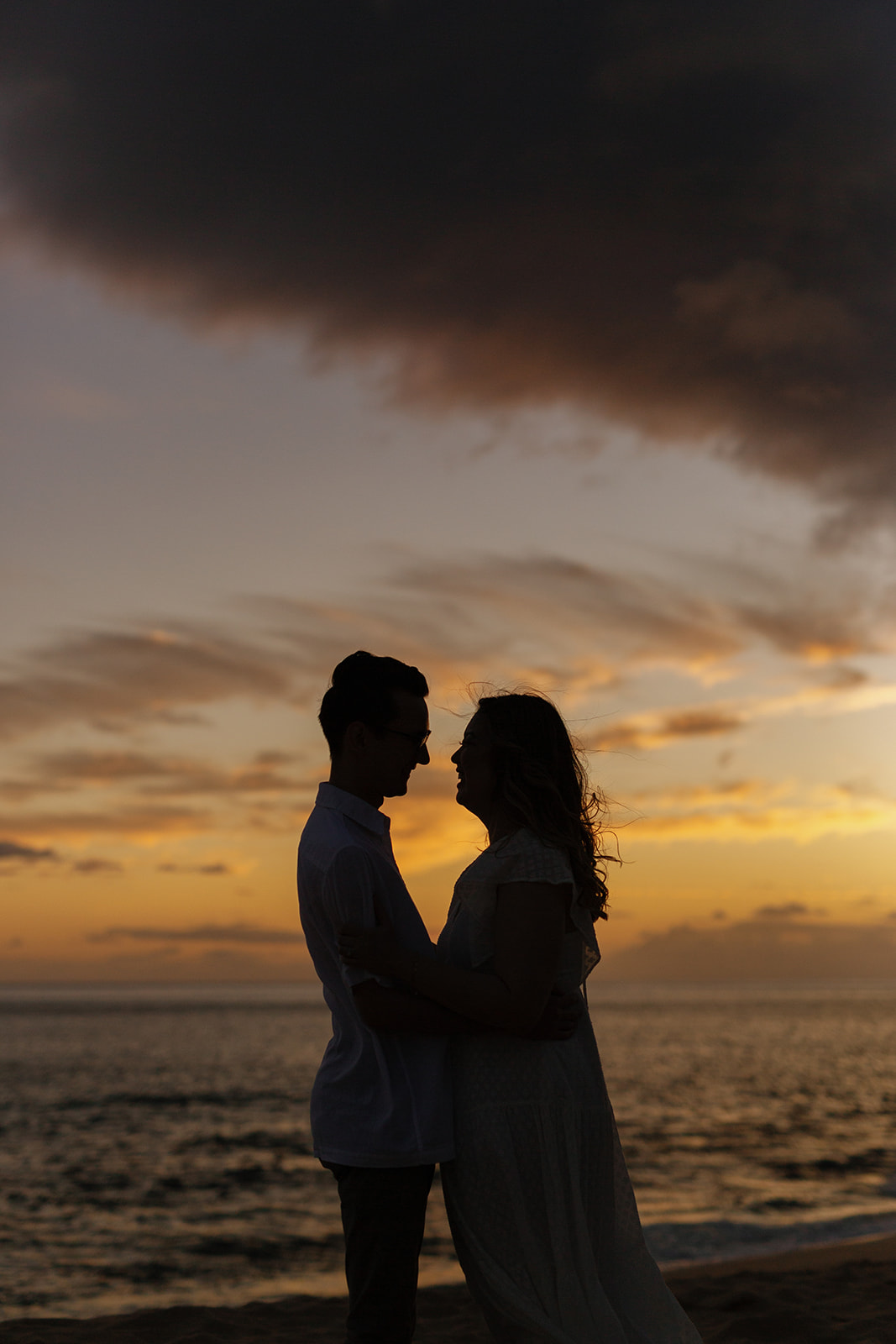 a couple taking sunset engagement photos on the beach in hawaii