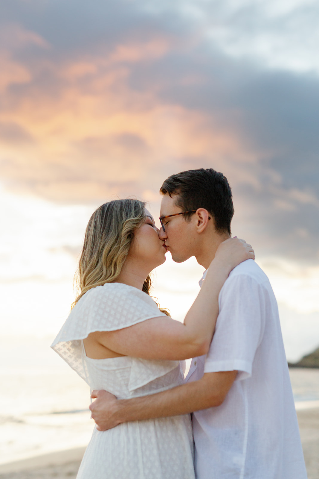 a couple kissing at sunset on the beach for their engagement session in hawaii