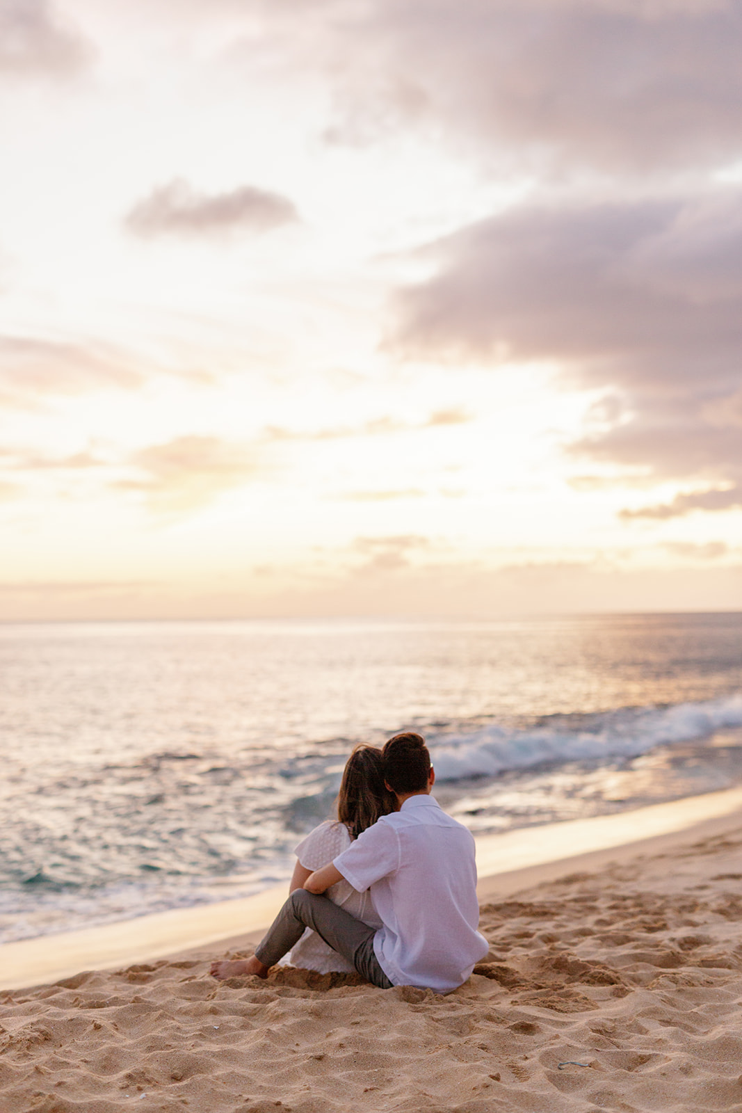 a couple sitting in the sand watching the sunset during their engagement session