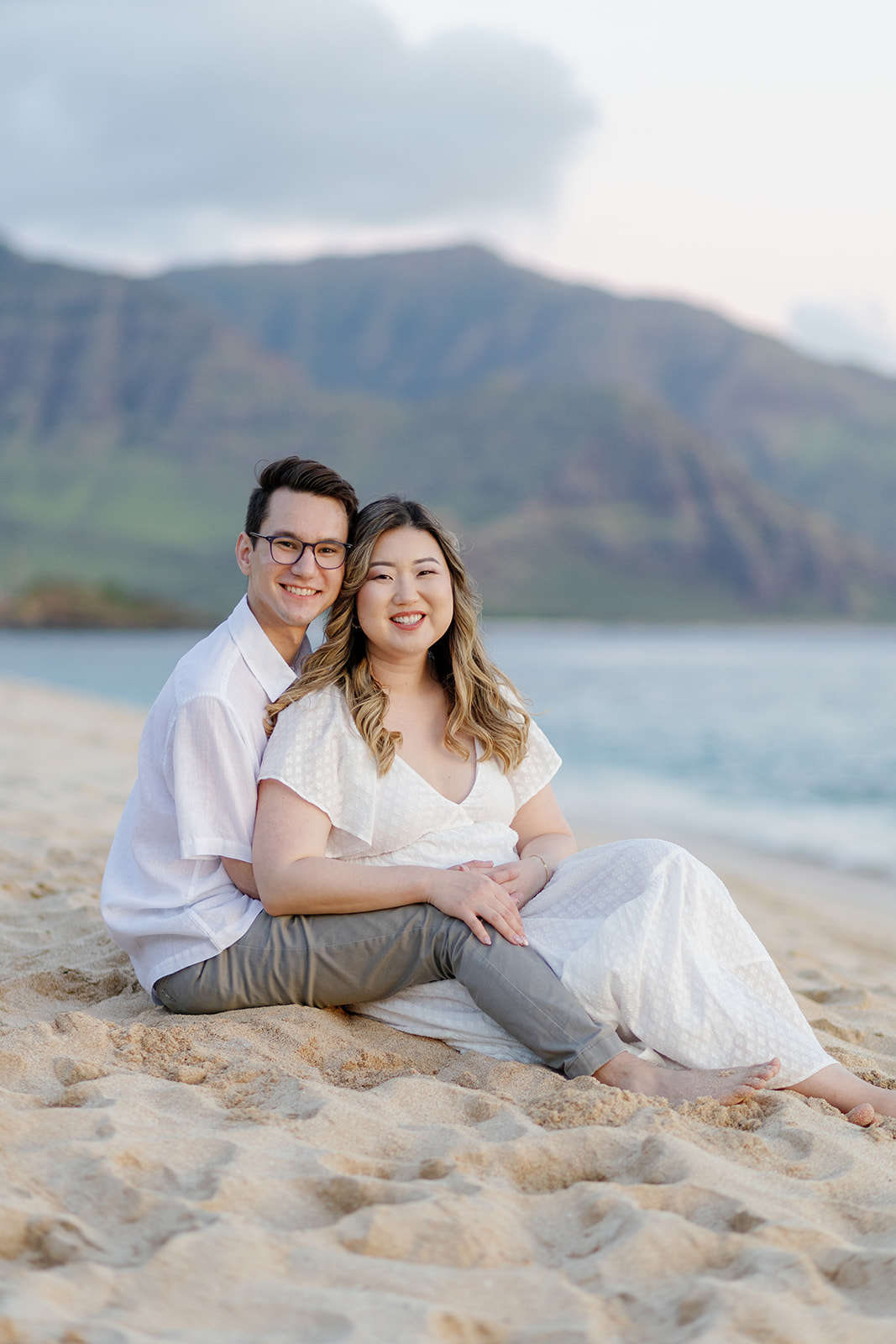a couple sitting in the sand on the beach in hawaii for their engagement session
