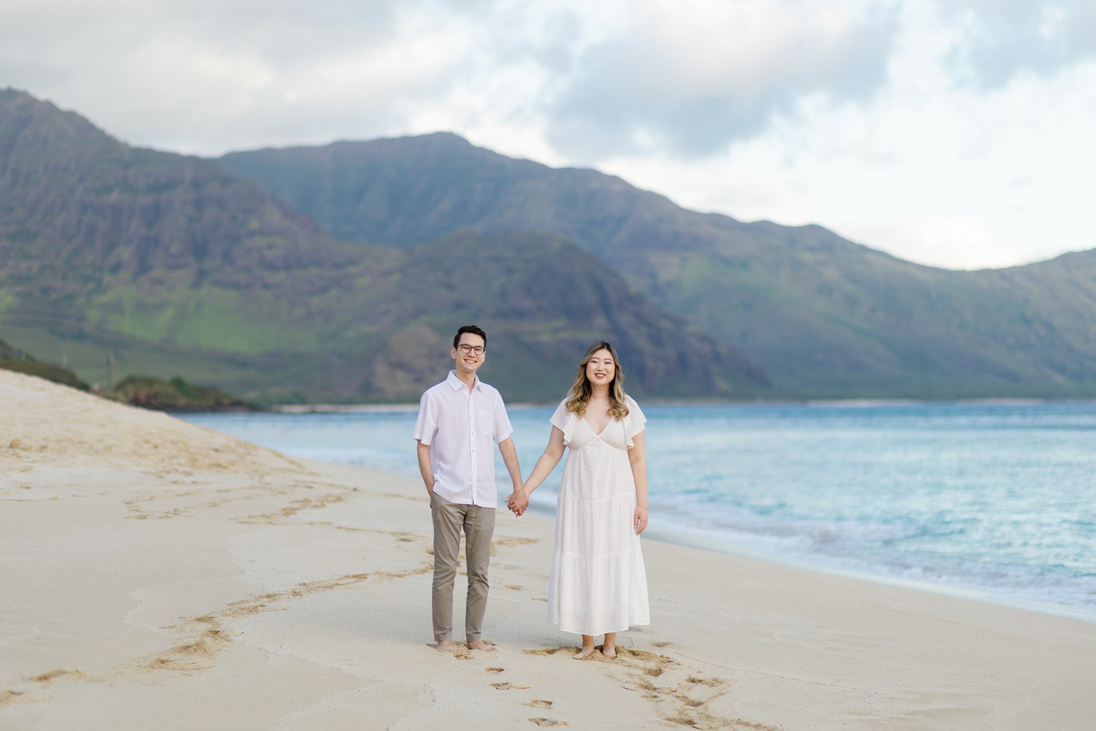 a couple standing in the sand holding hands and smiling during their engagement session