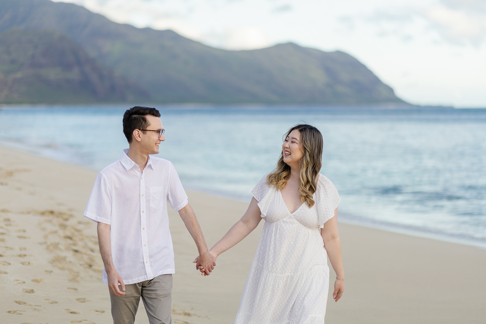 a couple holding hands and walking through the sand laughing with one another during their engagement session