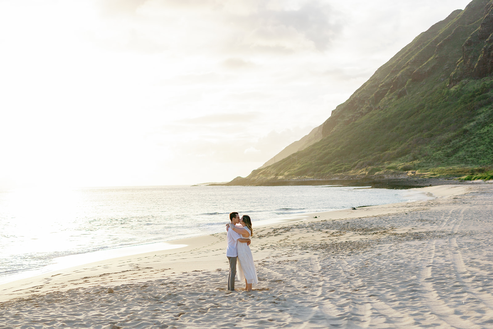 a couple kissing each other on the beach in hawaii at sunset for their engagement session