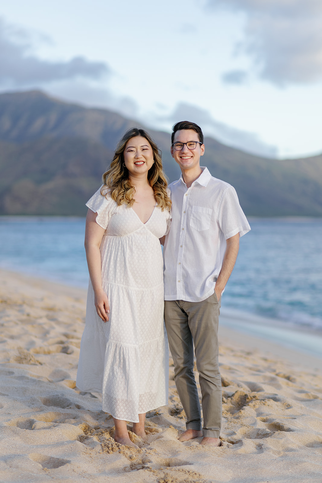 a couple posing for their engagement session in the sand next to the ocean